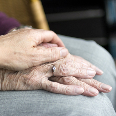 Hand einer jüngeren Person liegt auf Hand einer alten Frau.